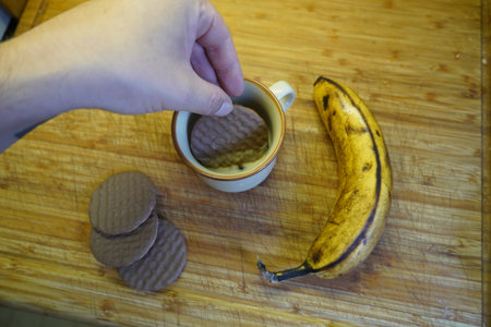 Man's hand taking a cup of coffee with chocolate cookies and bananaの写真素材
