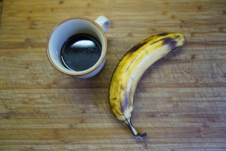A cup of coffee and a banana on a wooden board. Top view.の写真素材