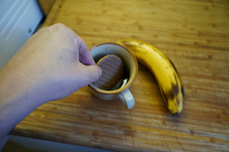 A woman's hand holds a cup of coffee and a banana on a wooden tableの写真素材