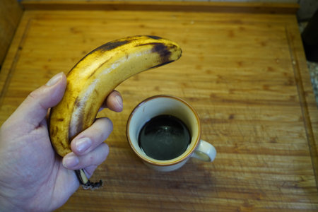 A man's hand holds a banana and a cup of coffee.の写真素材