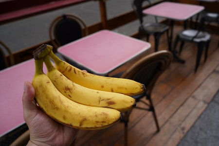 Bananas in hand on the background of tables and chairs of a cafeの写真素材