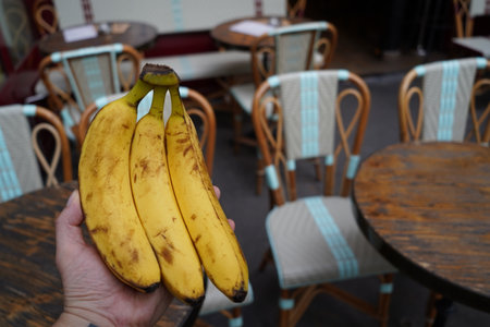 Bunch of bananas in hand on a background of tables and chairsの写真素材