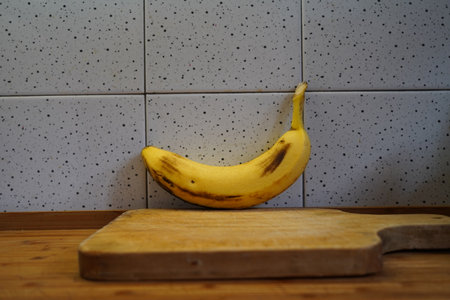 Banana on a wooden cutting board in front of a kitchen wallの写真素材