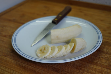 Peeled banana on a white plate with a knife on a wooden boardの写真素材