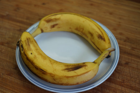 Ripe bananas in a plate on a wooden table, close-upの写真素材