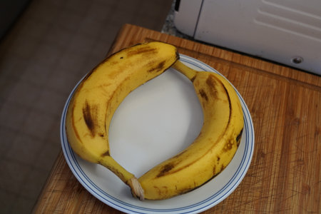 Banana on a white plate on a wooden cutting board in the kitchenの写真素材