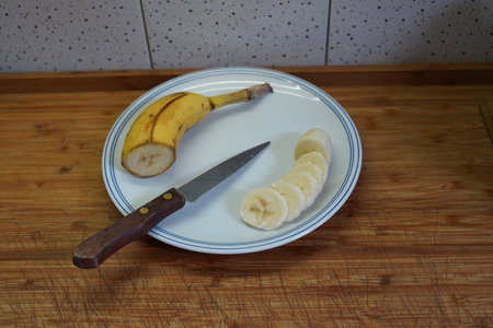 Sliced banana on a plate with knife on a wooden tableの写真素材