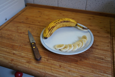 Banana and banana slices on a plate with knife on a wooden tableの写真素材