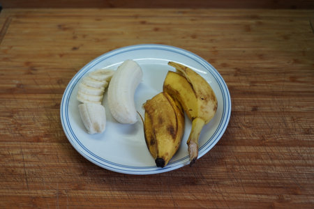 Banana and banana slices on a white plate on a wooden tableの写真素材