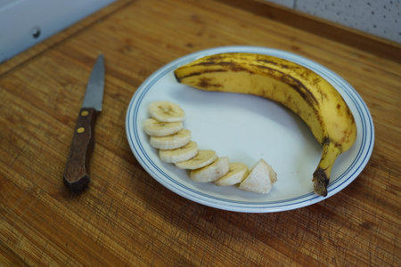 Sliced banana on a white plate with a knife on a wooden tableの写真素材