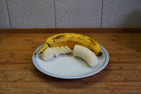 Banana and banana slices on a white plate on a wooden tableの写真素材