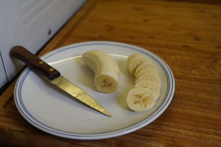 Banana slices on a plate with a knife in the kitchen.の写真素材