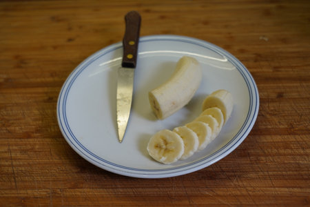 Banana slices on a plate with knife on a wooden table.の写真素材