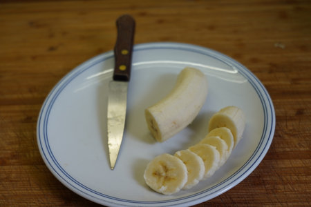 Banana slices on a plate with a knife on a wooden tableの写真素材