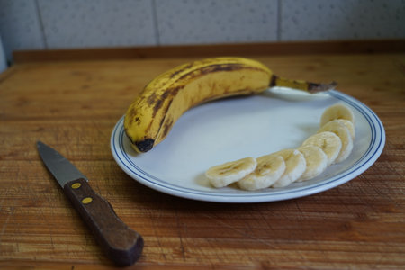 Banana and banana slices on a white plate with a knife.の写真素材