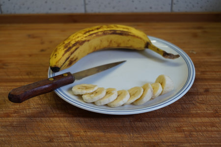 Banana slices on a plate and knife on a wooden table.の写真素材