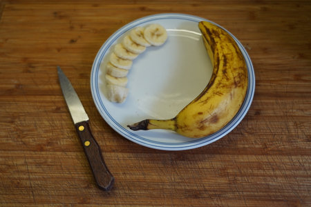 Sliced banana on a plate and knife on a wooden tableの写真素材