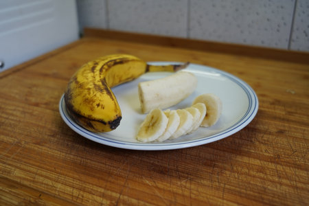 Banana slices on a white plate on a wooden table in the kitchenの写真素材