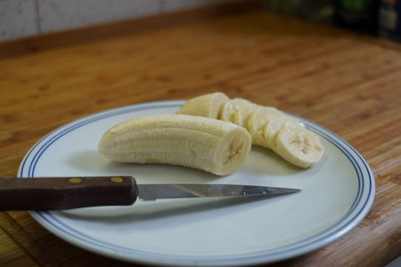Peeled banana on a plate with a knife on a wooden tableの写真素材
