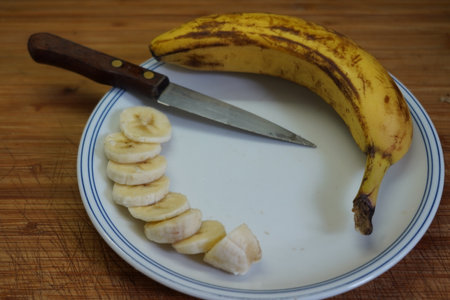 Sliced banana on a plate with a knife on a wooden tableの写真素材