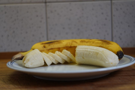 Banana on a white plate on a wooden table in the kitchenの写真素材