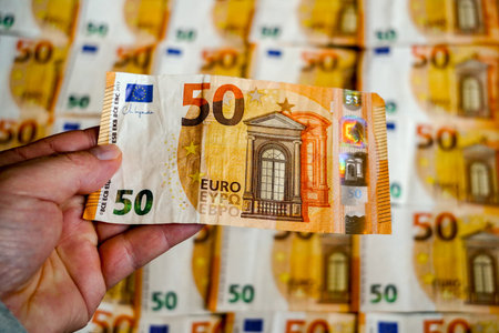 Man's hand holding fifty euro banknote on background of euro billsの写真素材
