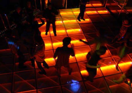 Disco Style Dance Hall with a group of people dancing on one side and a couple dancing on the other.  Cool patterned lighting on the dance floor.の写真素材