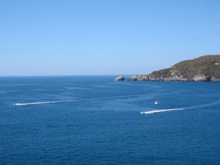 Two Jet skis race by a boat in Zihuatanejo bay on a clear day in Mexicoの写真素材
