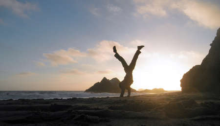 Man does handstand on the Ocean beach during a sunset splitting his legss to balanceの写真素材