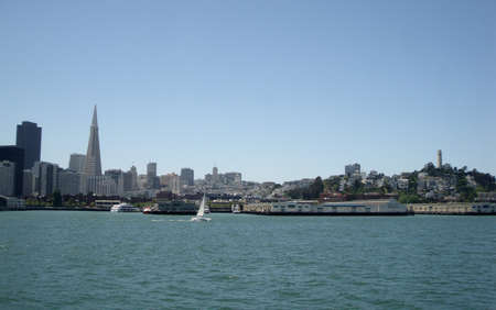 San Franscisco Bay with the area between the landmarks of TransAmerica building and Coit Tower in the background.  A sail boat passes by in the foreground taken from a ferryの写真素材