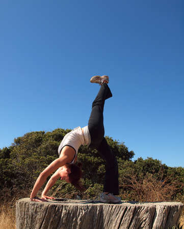 Attractive 20-something lady does a backbend on old tree stump while lifting leg to the sky on Angel Island in San Francisco Bay.の写真素材