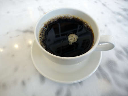 Cafe cup of Coffee on plate with windows above reflecting in the brew sitting on a granite table.の写真素材