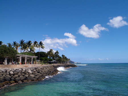 Wave crashes against rock seawall at Kaka`ako Waterfront Park with Waikiki in the distance.の写真素材