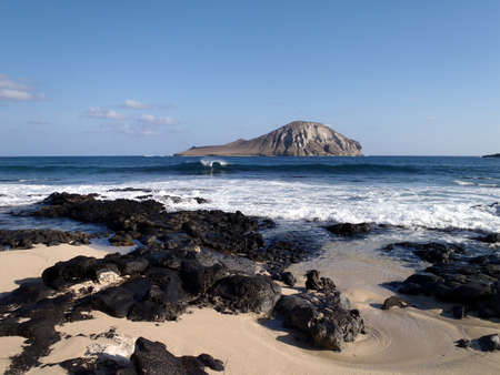 Wave crashing at rocky Baby Makapuu beach with Rabbit Island in the Distanceの写真素材