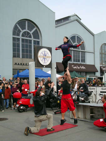SAN FRANCISCO- JANUARY 16: English Circus performers put on a show as a man balances his sister on his shoulders tries to pass her to a man squatting from crowd January 16, 2010 at Ferry Building San Francisco. のeditorial素材