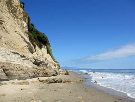 Waves lap on the beach next to tall cliff in Santa Barbara, California の写真素材