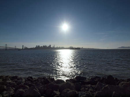 Sunset Over San Francisco Cityscape and Bay with tugboat pulling cargo boat seen from rocky shore of Treasure Island in California の写真素材