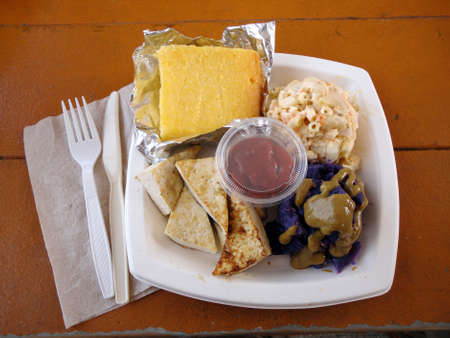 Tofu Slices, Sweet Potato, corn bread, and mac salad on a square plate and plastic fork and knife on a picnic table                                の写真素材