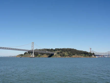 Two sides of the iconic Bay Bridge, the new tower under construction, yerba buena island, tugboat and the East Bay on a nice day in California.                               の写真素材