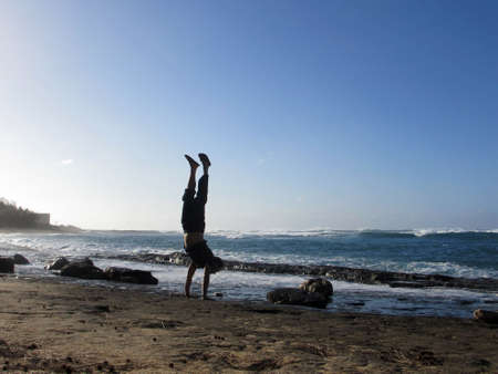 Man Handstanding on lava rocks on the beach as wave crash on the North Shore of Oahu, Hawaii.                    の写真素材