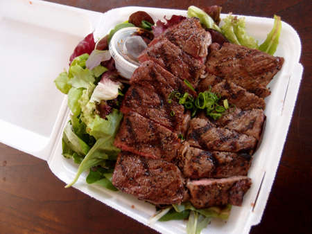 Steak with Salad on a to go Styrofoam plate on a wood table.の写真素材