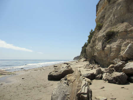 Waves lap on the beach with large rocks next to tall cliff in Santa Barbara, California.の写真素材