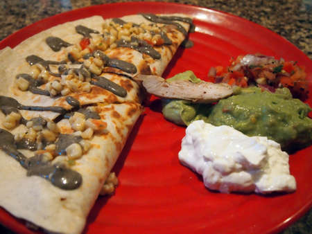 Chicken Quesadilla with corn and sauce on top and sour creme guacamole, and pico de gallo on a red plate.の写真素材