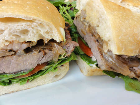 Steak Sandwich Close-up on Sourdough with lettuce and tomatoes on a white plate.                 の写真素材