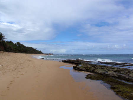 Beach with rocks in the water and foot prints in the sand, San Juan, Puerto Rico on a beautiful day with waves lapping on the beach.の写真素材