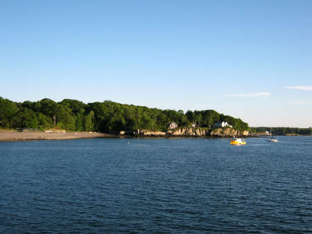 Beach, house on island shore and boats in the waters of Portland Harbor in Maine.の写真素材
