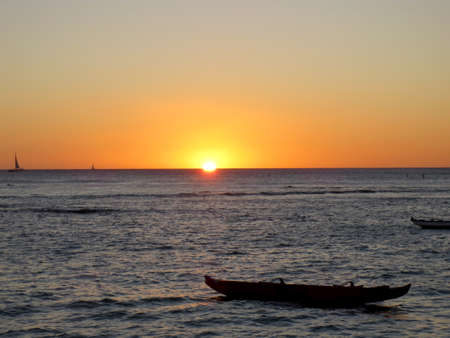 Sunset on the horizon of the Pacific Ocean with  canoes, and boats resting in the waters off the shore of Waikiki on Oahu.の写真素材