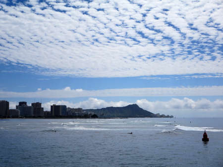 Waves roll in in front Waikiki and iconic Diamondhead in the distance during a beautiful day with amazing clouds on the island of Oahu, Hawaii.の写真素材