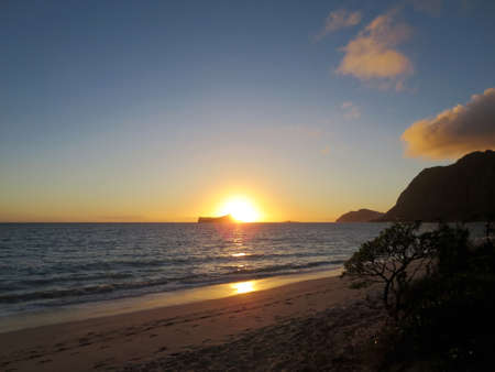 Early Morning Sunrise on Waimanalo Beach over Rabbit Island bursting over the island on Oahu, Hawaii.  With Lighthouse on mountain in distance.の写真素材