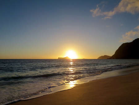 Early Morning Sunrise on Waimanalo Beach over Rabbit Island bursting over the island on Oahu, Hawaii.  With Lighthouse on mountain in distance.の写真素材